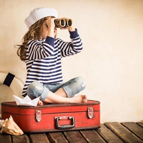 Happy kid playing with toy sailing boat indoors. Travel and adventure concept