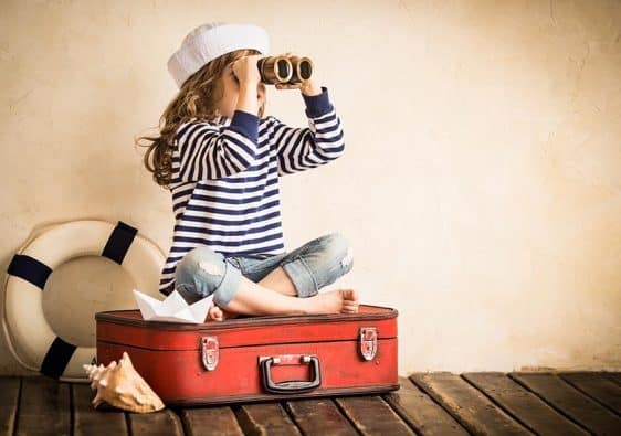 Happy kid playing with toy sailing boat indoors. Travel and adventure concept