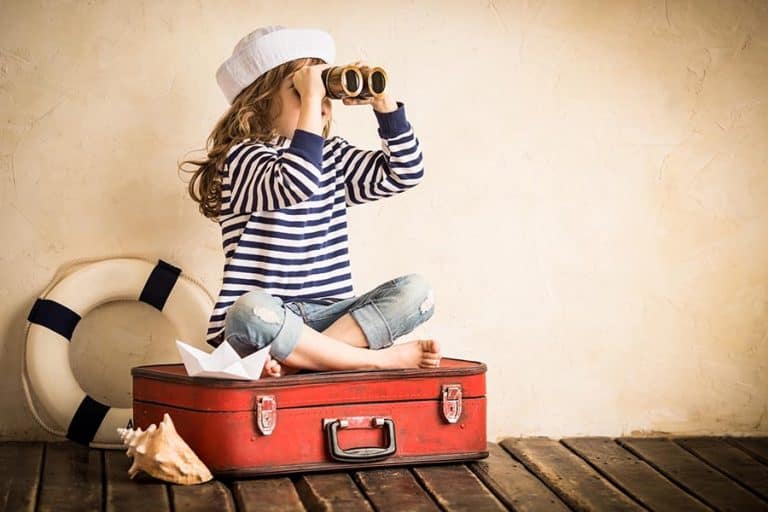 Happy kid playing with toy sailing boat indoors. Travel and adventure concept