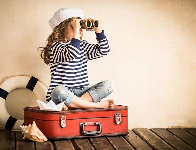 Happy kid playing with toy sailing boat indoors. Travel and adventure concept