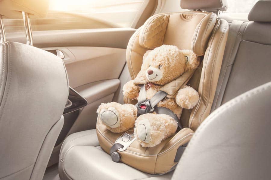 Baby child seat car. A beige teddy bear is fastened with seat belts in a car seat. Travel by car.