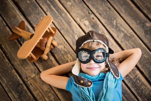 Child pilot with vintage plane toy on grunge wooden background