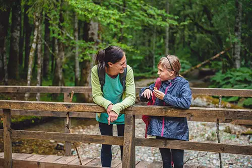 Mother and daughter with dog resting on wooden bridge in the mountain forest