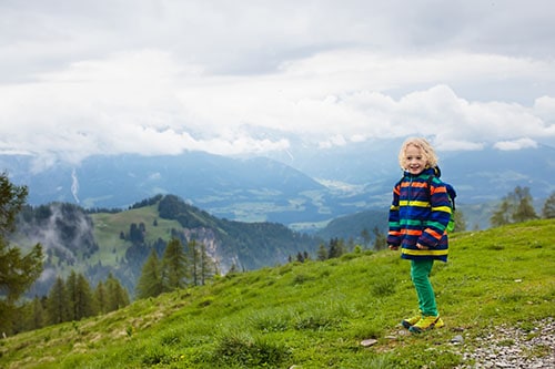 Children hiking in Alps mountains. Kids look at snow covered mountain in Austria. Spring family vacation. Little boy on hike trail in blooming alpine meadow. Outdoor fun and healthy activity.