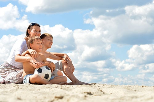 mum and sons sitting on the beach with a football