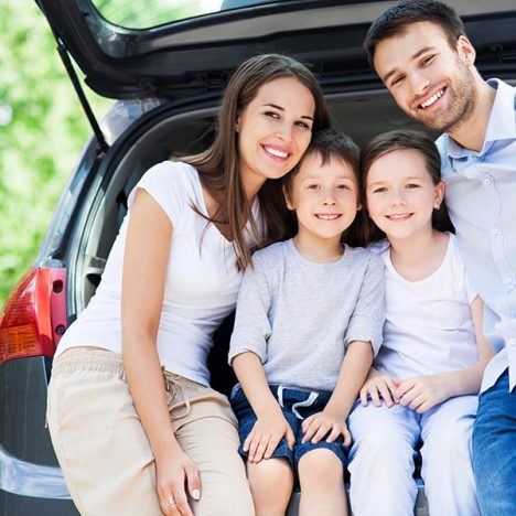 Family sitting in car boot smiling.