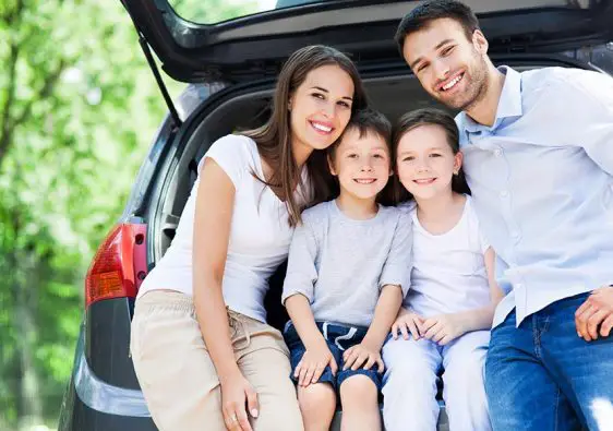 Family sitting in car boot smiling.