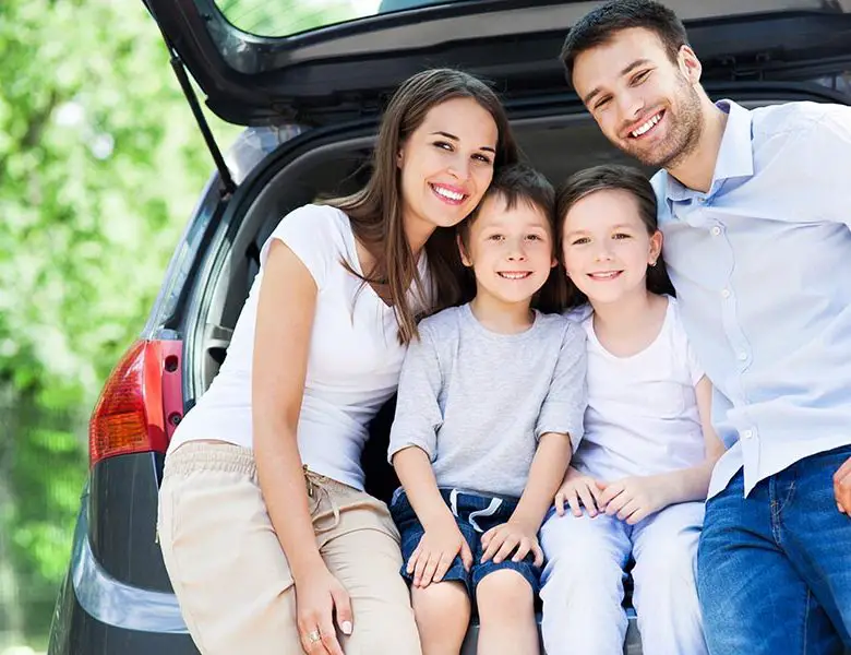 Family sitting in car boot smiling.