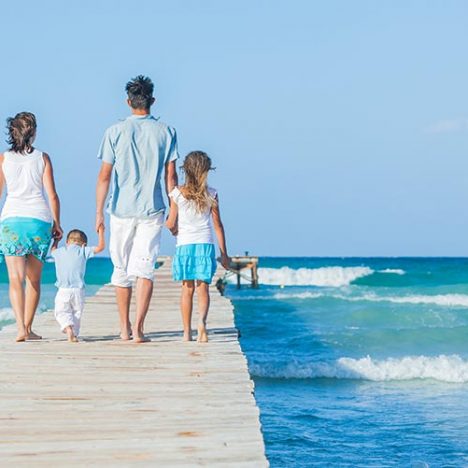 Family of four on wooden jetty by the ocean. Back view