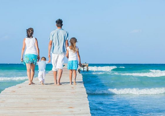 Family of four on wooden jetty by the ocean. Back view