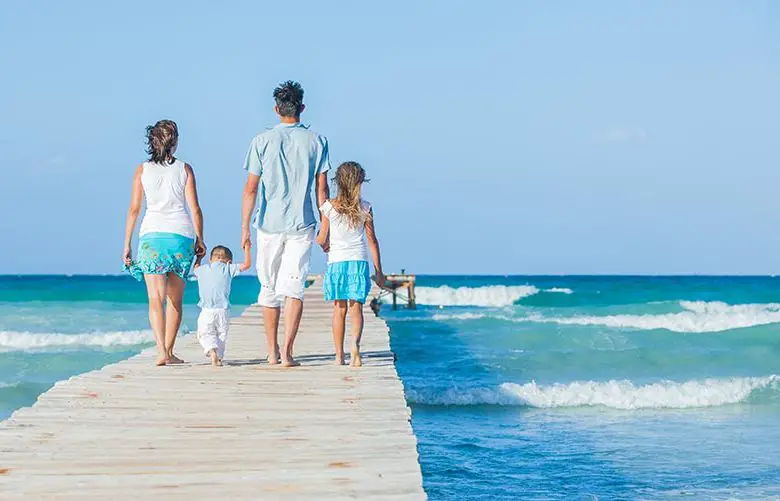 Family of four on wooden jetty by the ocean. Back view