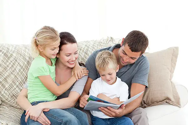 Adorable father and son reading a book to their family sitting in the living-room