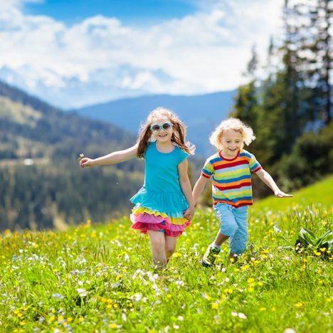 Children hiking in Alps mountains. Kids run at snow covered mountain in Austria. Spring family vacation. Little boy and girl on hike trail in blooming alpine meadow. Outdoor fun and healthy activity.