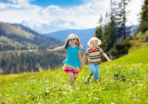 Children hiking in Alps mountains. Kids run at snow covered mountain in Austria. Spring family vacation. Little boy and girl on hike trail in blooming alpine meadow. Outdoor fun and healthy activity.