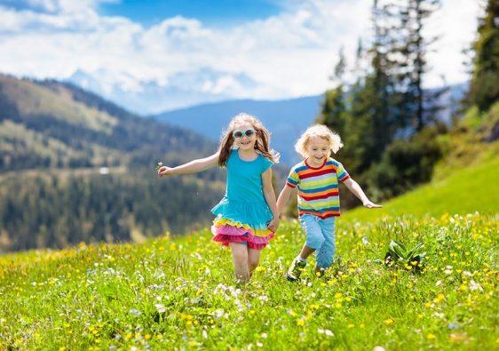 Children hiking in Alps mountains. Kids run at snow covered mountain in Austria. Spring family vacation. Little boy and girl on hike trail in blooming alpine meadow. Outdoor fun and healthy activity.