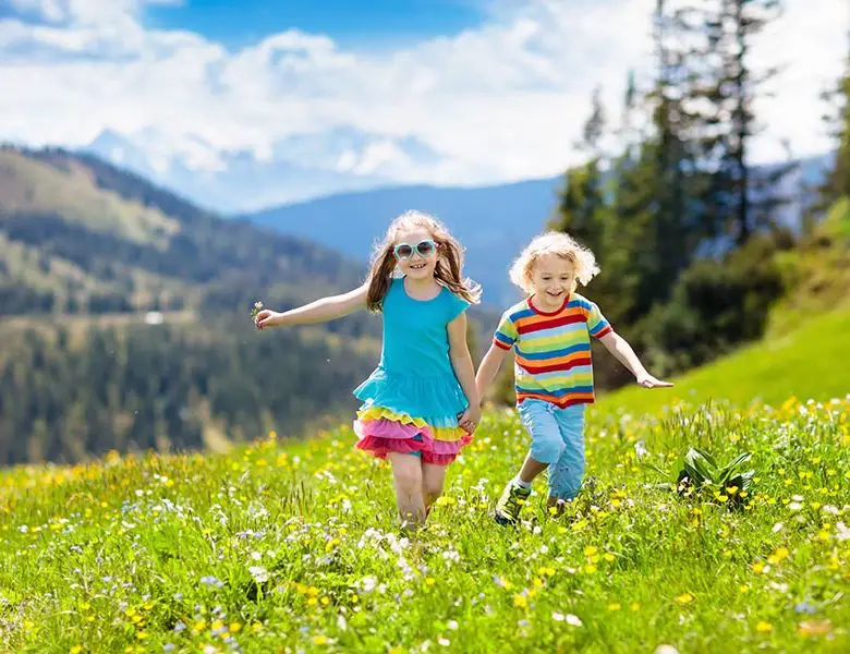 Children hiking in Alps mountains. Kids run at snow covered mountain in Austria. Spring family vacation. Little boy and girl on hike trail in blooming alpine meadow. Outdoor fun and healthy activity.